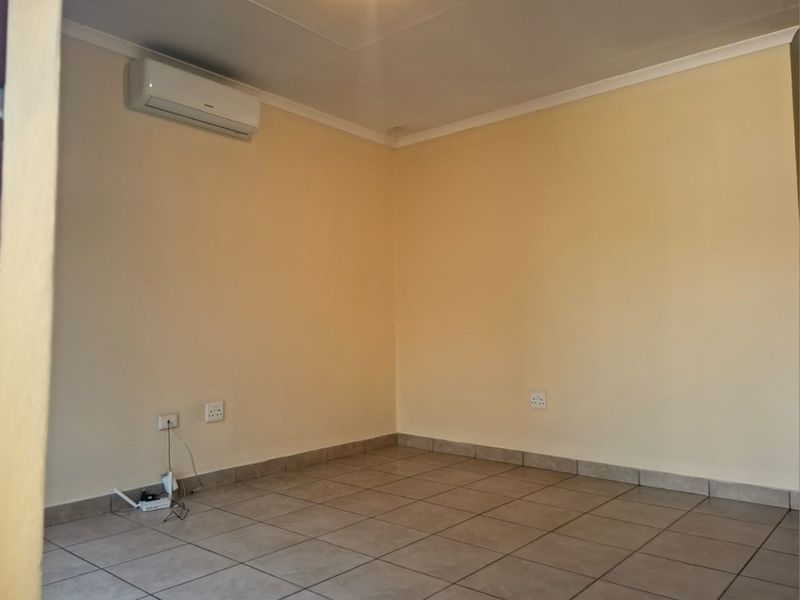 An empty living room featuring tiled flooring, neutral walls, and a wall-mounted split-system air conditioning unit.