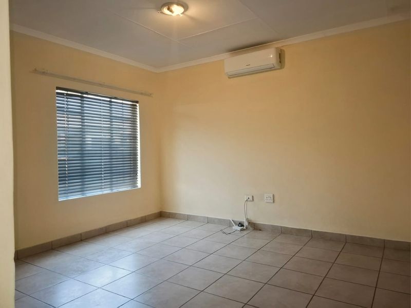 A clean, empty bedroom featuring tiled flooring, an installed air conditioning unit, and venetian blinds, providing a neutral space ready for personalization.