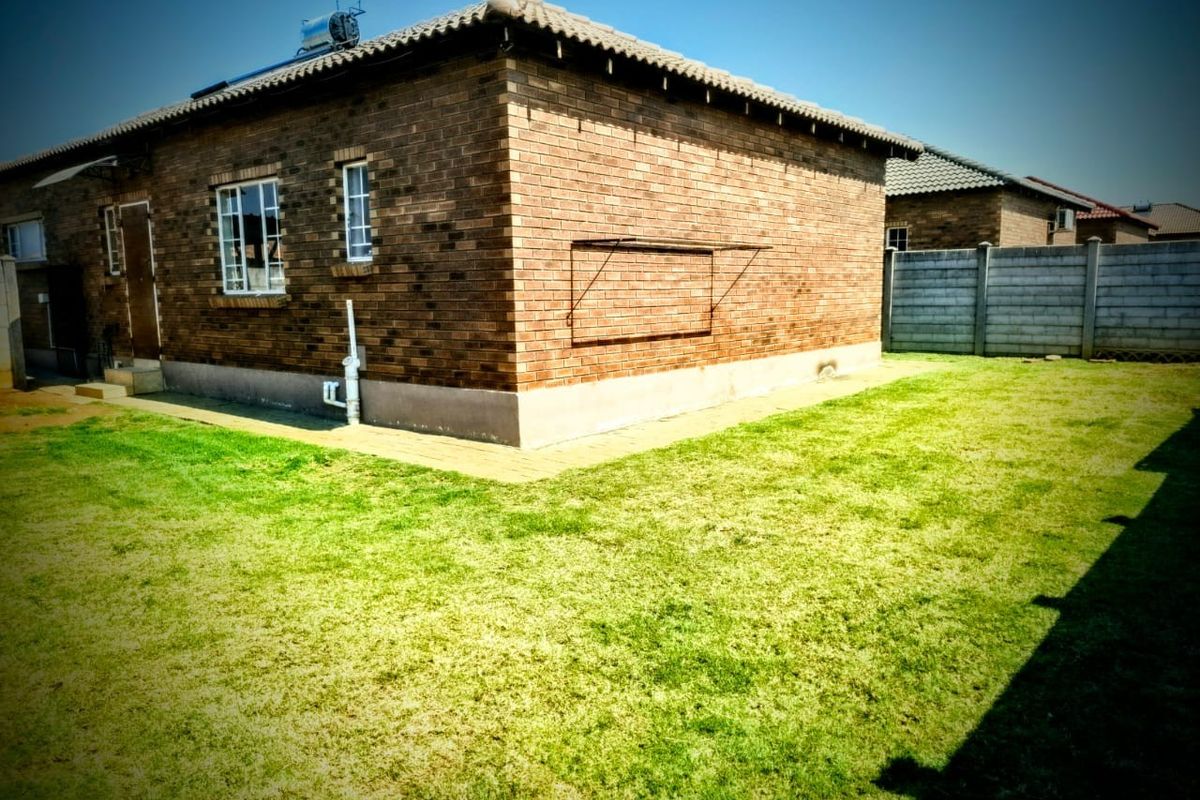 Rear view of a face brick house featuring a tiled roof, solar water heater, and a well-maintained lawn with a precast boundary wall.