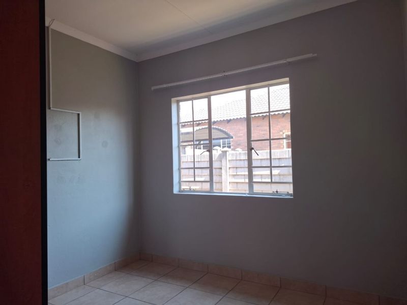 A vacant bedroom featuring neutral grey walls, tiled flooring, and a window fitted with security bars.