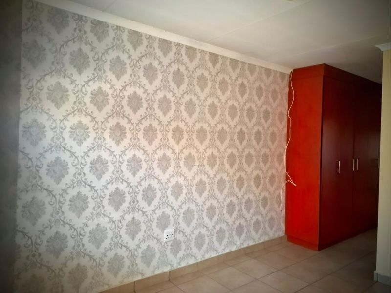 A bedroom featuring tiled flooring, a built-in wardrobe, and patterned wallpaper, currently presented as an empty space.