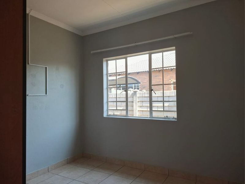 An empty bedroom featuring neutral grey walls, tiled flooring, and a window with security bars, providing a blank canvas for personalization.