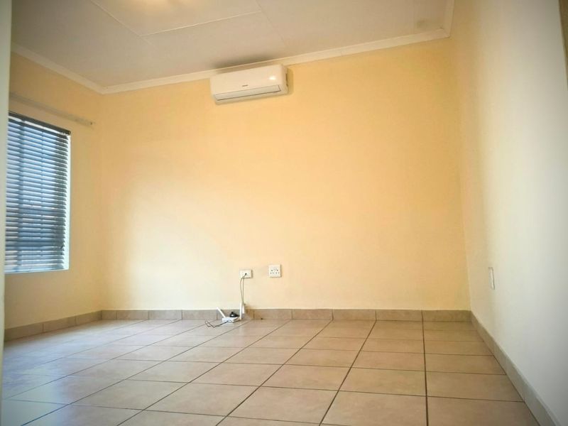 A clean, empty bedroom featuring tiled flooring, an installed air conditioning unit, and venetian blinds, providing a neutral canvas for personalization.