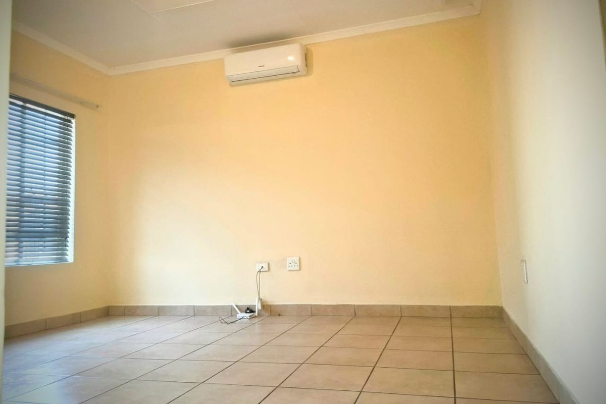 A clean, empty bedroom featuring tiled flooring, an installed air conditioning unit, and venetian blinds, providing a neutral canvas for personalization.