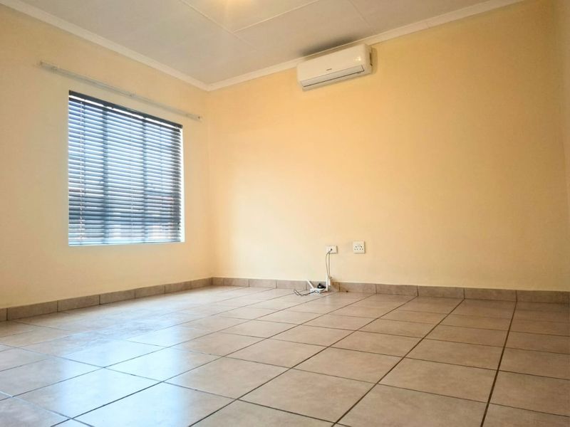 A clean, empty bedroom featuring neutral tiled flooring, an installed air conditioning unit, and venetian blinds on the window.