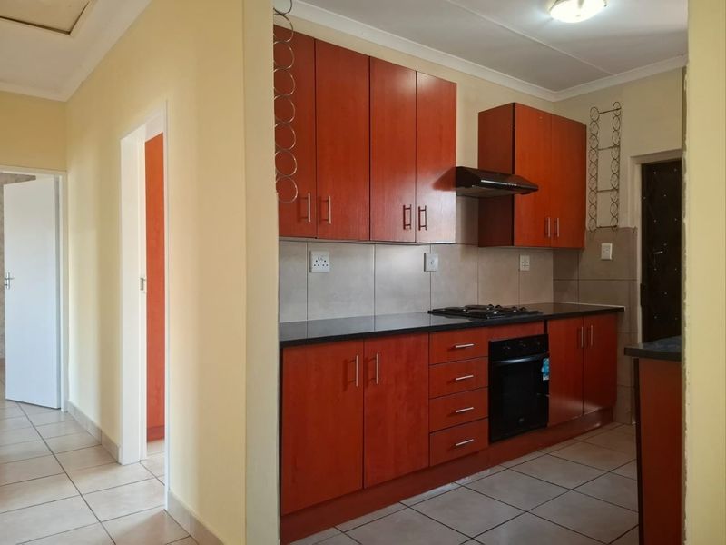 A functional kitchen featuring warm-toned built-in cabinetry, black granite countertops, a built-in oven, gas hob, and tiled flooring throughout.