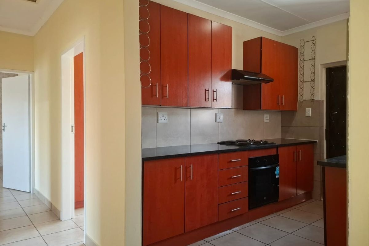 A functional kitchen featuring warm-toned built-in cabinetry, black granite countertops, a built-in oven, gas hob, and tiled flooring throughout.