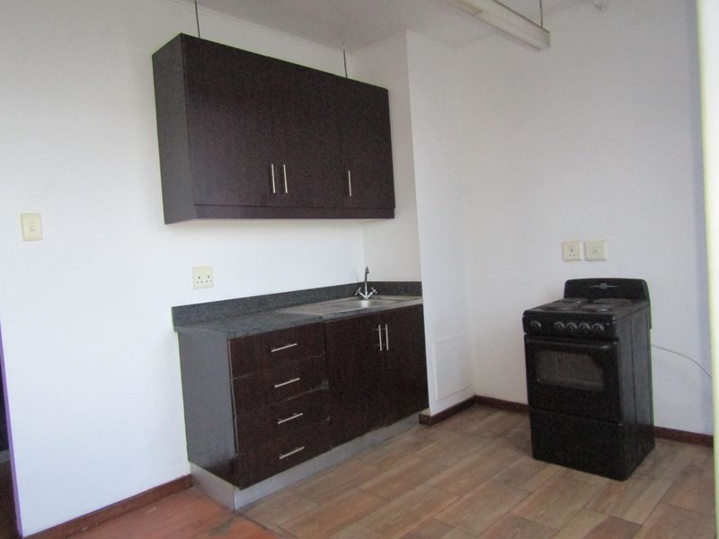 A compact kitchen featuring dark wood cabinetry, stone countertops, a stainless steel sink, and a freestanding stove with tiled flooring.