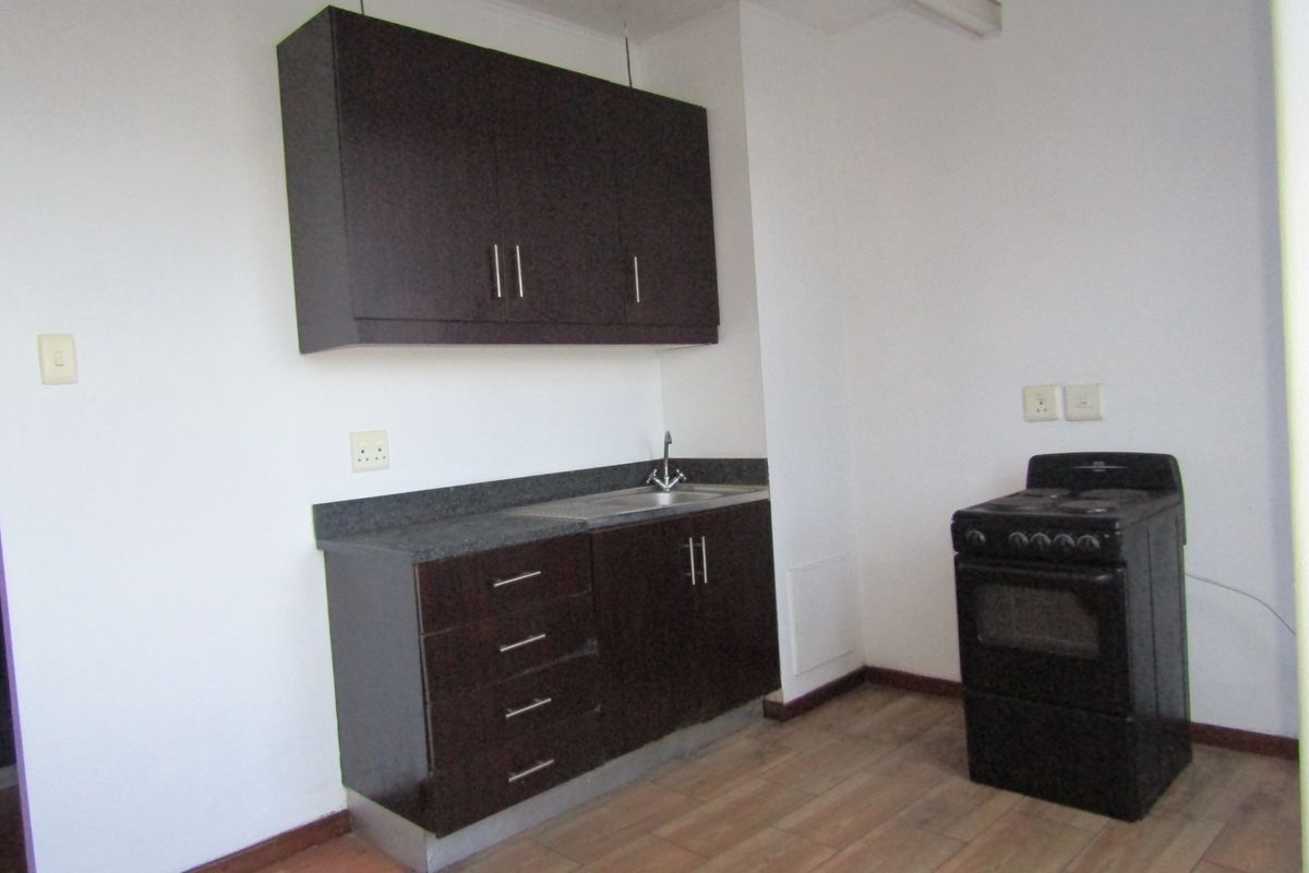 A compact kitchen featuring dark wood cabinetry, stone countertops, a stainless steel sink, and a freestanding stove with tiled flooring.