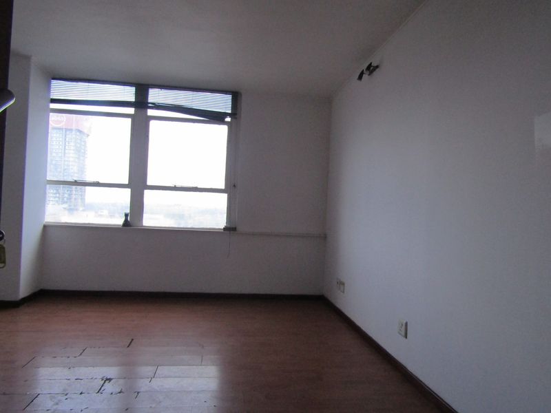 An empty living room featuring large windows with city views, laminate flooring, and neutral walls, offering a blank canvas for renovation.