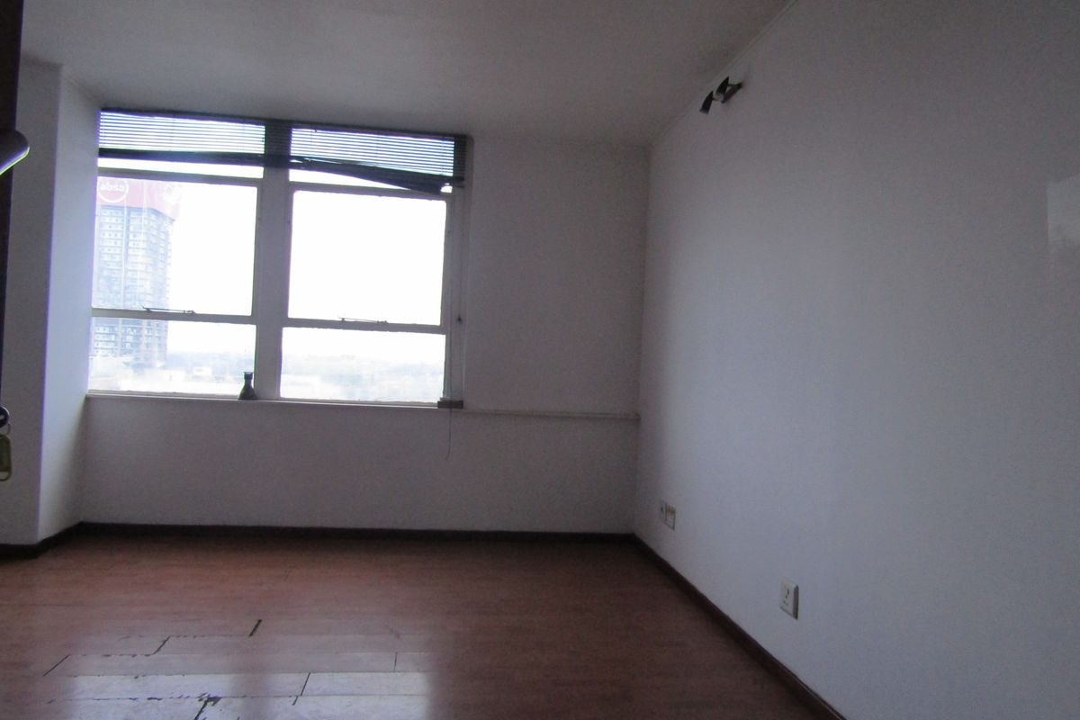An empty living room featuring large windows with city views, laminate flooring, and neutral walls, offering a blank canvas for renovation.