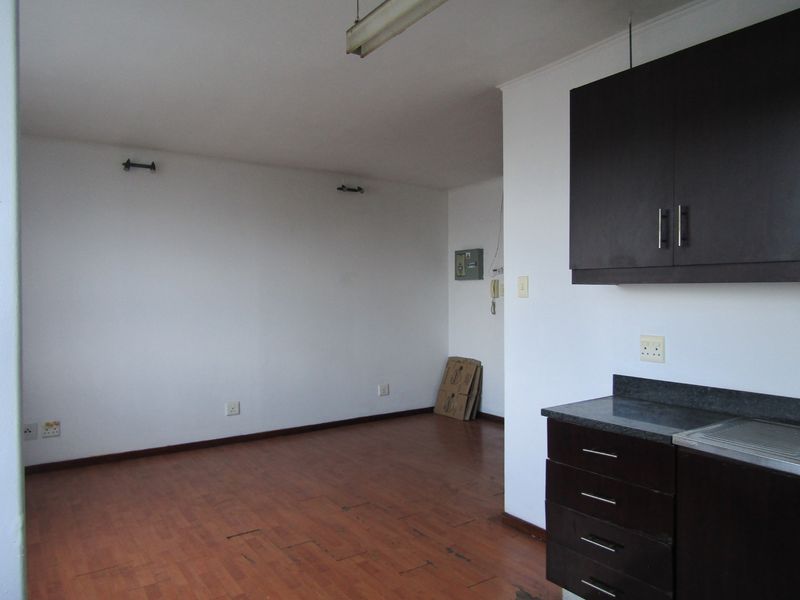 An open-plan living and kitchen area featuring dark cabinetry, stone countertops, and laminate flooring, presenting a blank canvas for potential renovation.