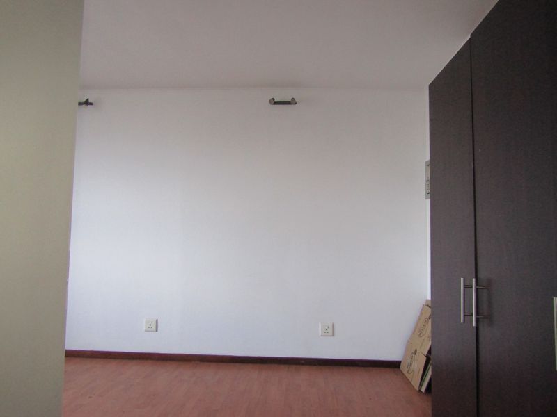 A clean, empty bedroom featuring laminate flooring and a built-in dark wood wardrobe, providing a blank canvas for personalization.