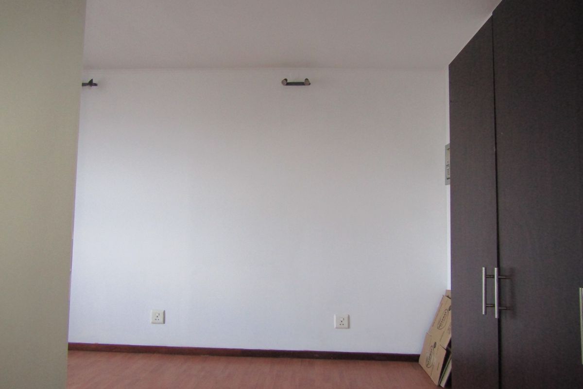 A clean, empty bedroom featuring laminate flooring and a built-in dark wood wardrobe, providing a blank canvas for personalization.