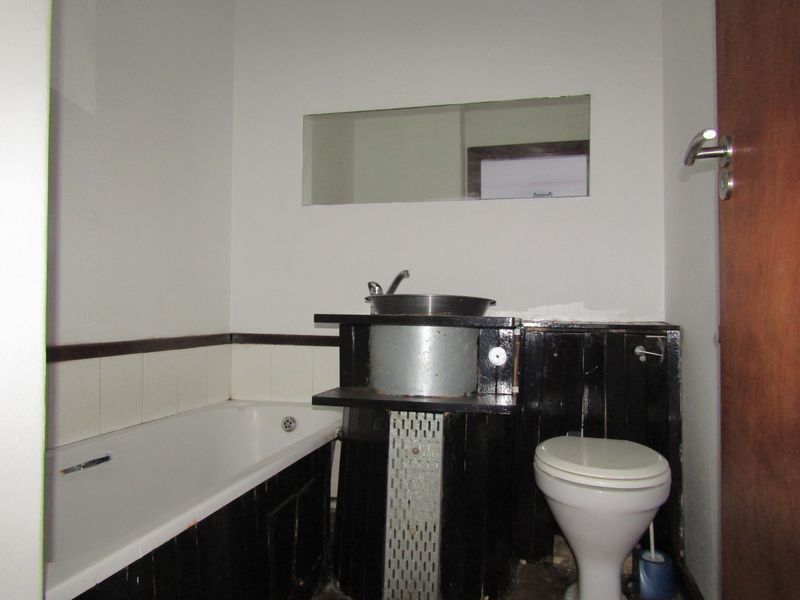 A dated bathroom featuring a bathtub, toilet, and basin with custom dark-painted cabinetry and a wall-mounted mirror.