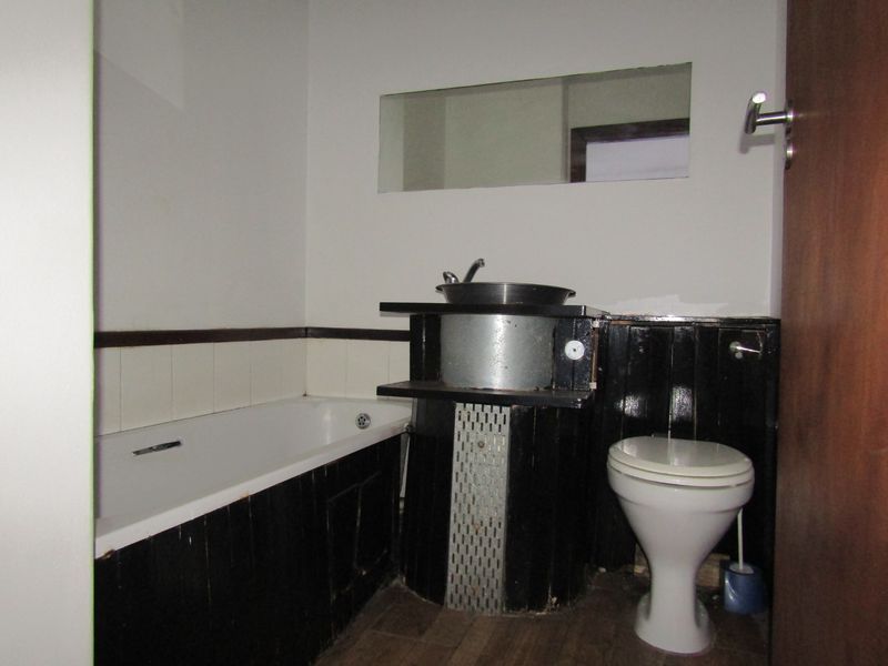 A dated bathroom featuring a bathtub, toilet, and basin with dark wood-paneled surrounds and a wall-mounted mirror.