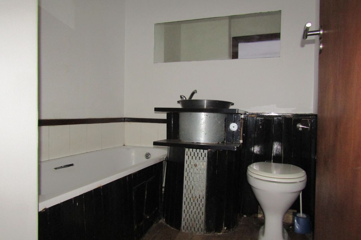 A dated bathroom featuring a bathtub, toilet, and basin with dark wood-paneled surrounds and a wall-mounted mirror.