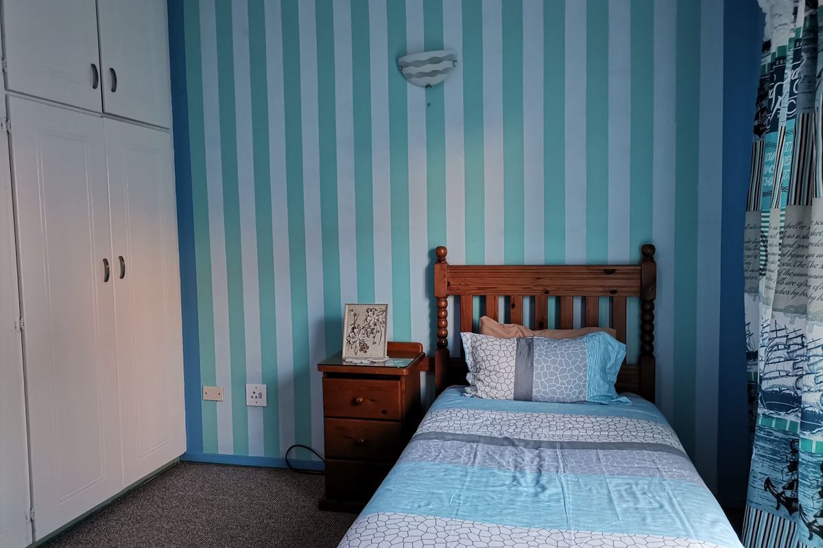 A bedroom featuring a built-in wardrobe, wall-mounted lighting, and striped wallpaper.