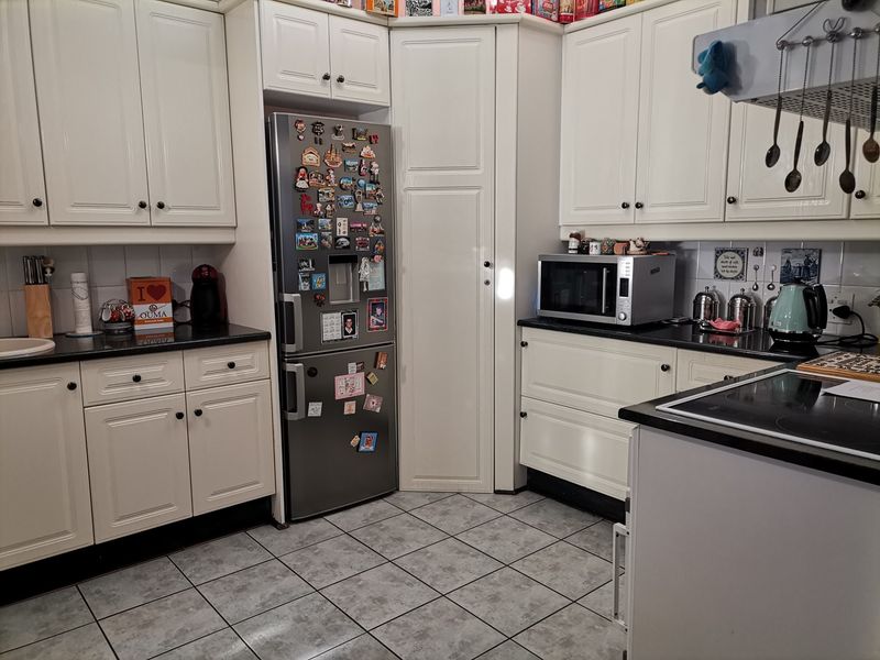 A functional kitchen featuring white cabinetry, black granite countertops, tiled backsplash, and ceramic floor tiles with an integrated hob and extractor fan.