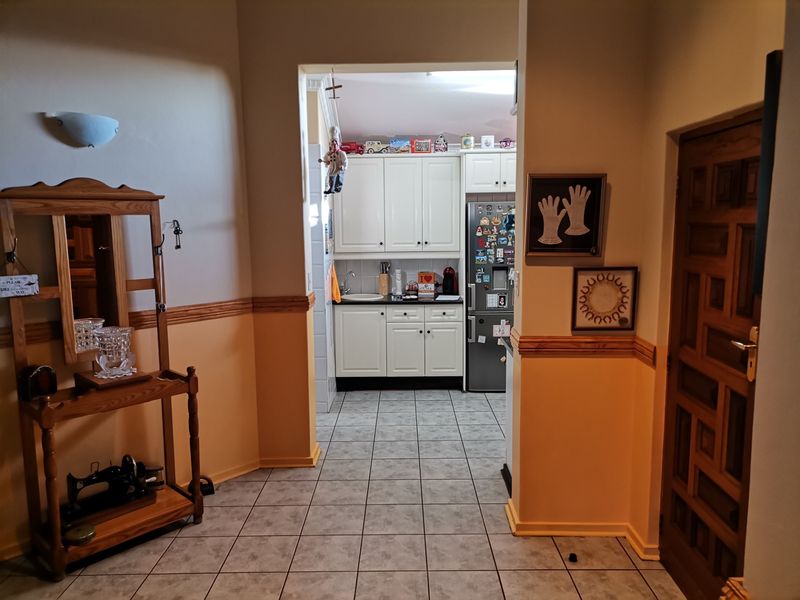 A view from a hallway into a kitchen featuring white cabinetry, tiled flooring, and a traditional wooden dado rail.