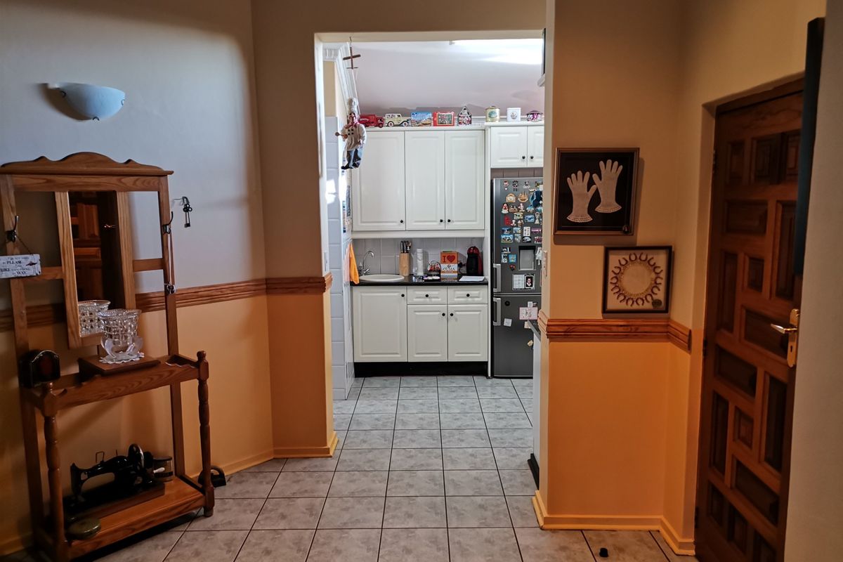 A view from a hallway into a kitchen featuring white cabinetry, tiled flooring, and a traditional wooden dado rail.