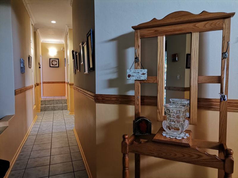 A well-lit hallway featuring tiled flooring, crown molding, and decorative chair rail trim, leading towards a raised transition area.