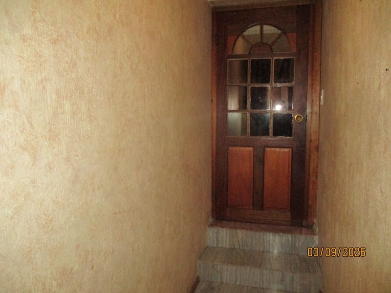 A narrow hallway featuring textured wall finishes, stone steps, and a traditional timber-framed glass door.