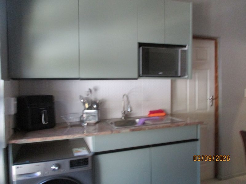 A compact kitchen area featuring built-in cabinetry, a stainless steel sink, stone countertops, and a built-in microwave.