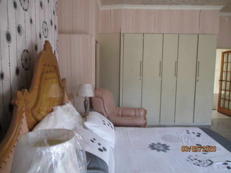 A bedroom featuring built-in cupboards and decorative coving, currently showing dated wallpaper and finishes that would benefit from a modern update.