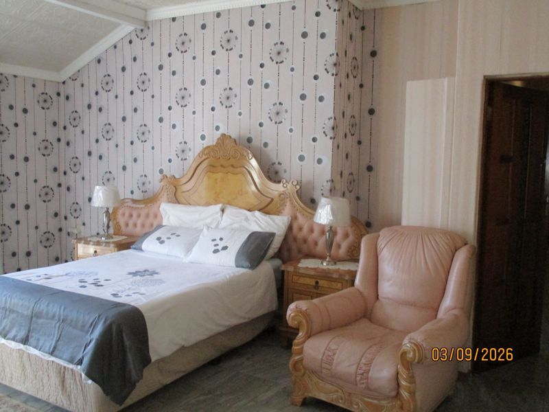 A bedroom featuring patterned wallpaper, a sloped ceiling with coving, and built-in architectural details.