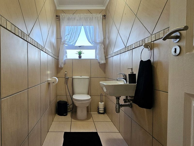A compact guest bathroom featuring floor-to-ceiling diamond-patterned wall tiles, a wall-mounted basin, and a standard toilet.