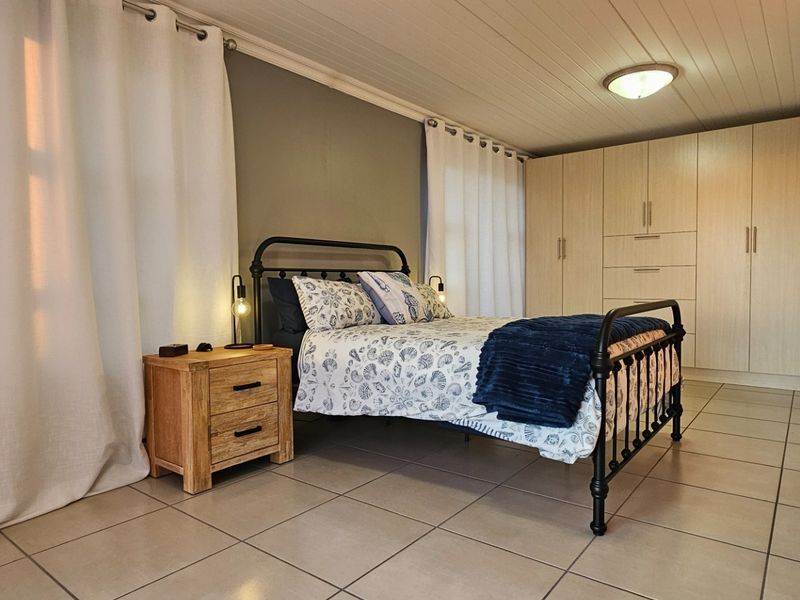 A well-maintained bedroom featuring neutral tiled flooring, extensive built-in cabinetry, and a classic tongue and groove ceiling finish.