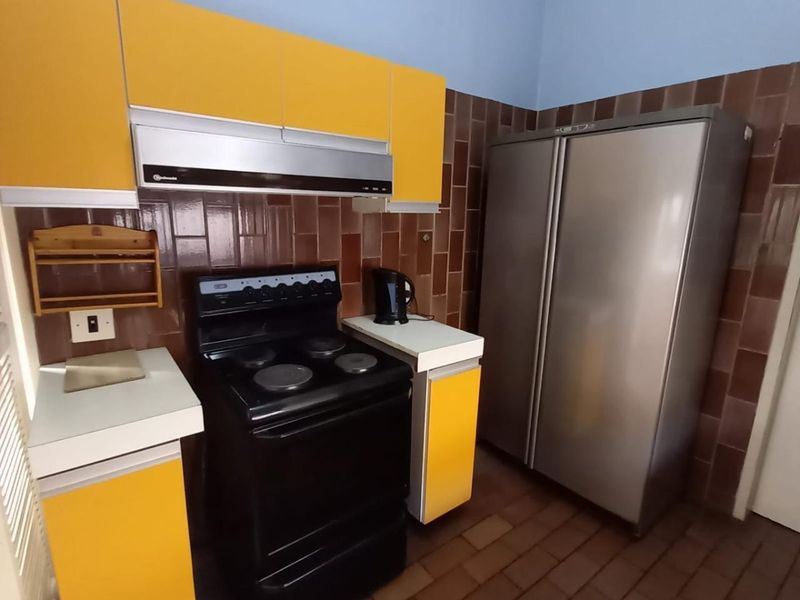 A functional kitchen featuring yellow cabinetry, a tiled backsplash, and tiled flooring, offering a dated aesthetic ready for modernization.