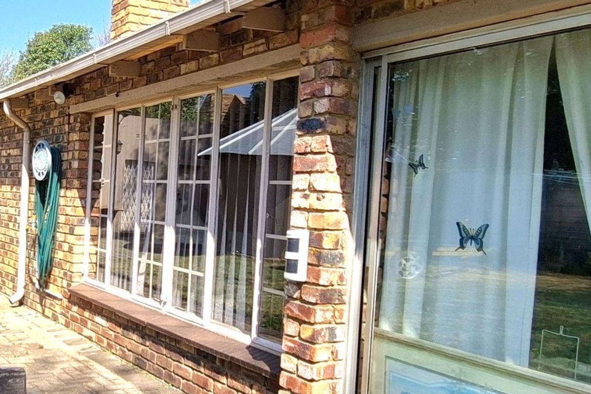 Rear exterior view of the house featuring face-brick walls, paved patio area, and large sliding glass doors.