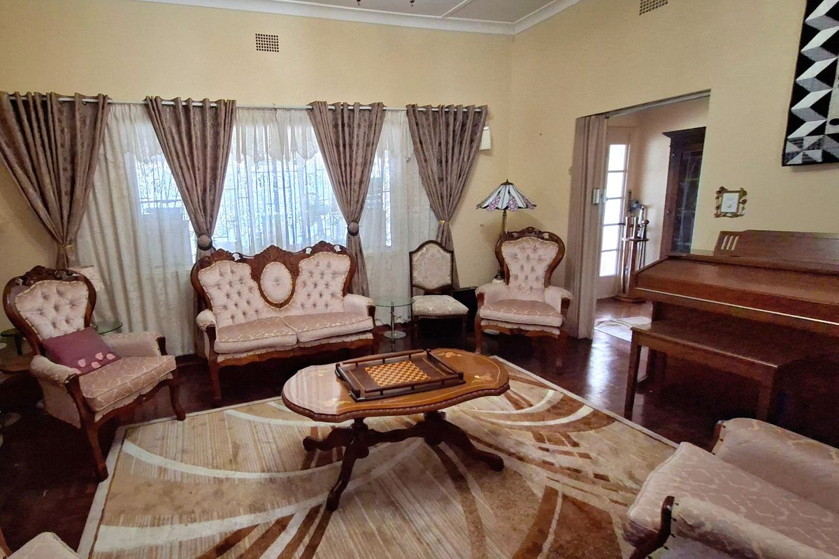 A traditional living room featuring hardwood flooring, decorative ceiling cornices, and large windows with curtains, offering a classic and spacious atmosphere.