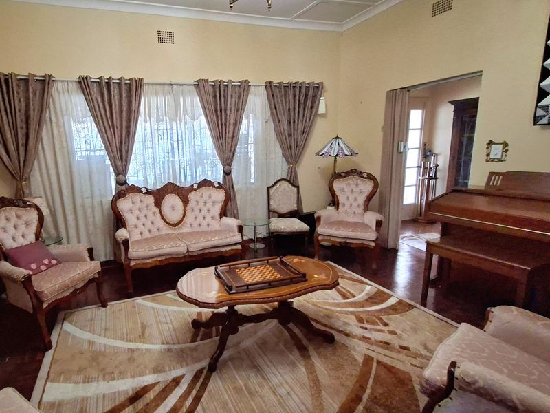 A traditional living room featuring hardwood flooring, decorative ceiling cornices, and large windows with curtains, offering a classic and spacious atmosphere.