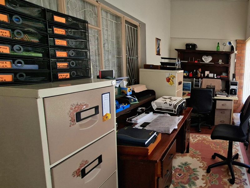 A functional home office space featuring security gates on the windows and a brick feature wall, providing a practical work environment.