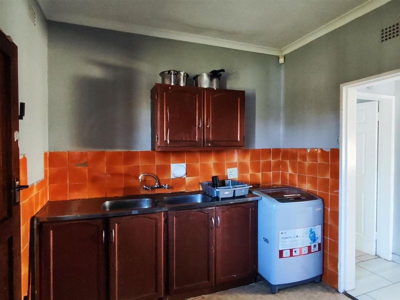 A functional laundry area featuring built-in wooden cabinetry, a double stainless steel sink, and vibrant orange tiled splashbacks.