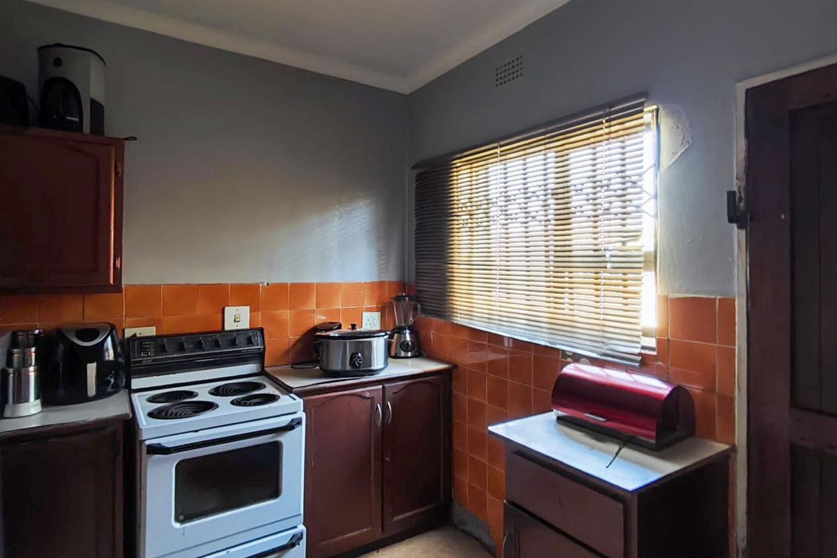 A compact kitchen featuring dark wood cabinetry, orange tiled splashbacks, and a freestanding stove, requiring some cosmetic updates to the wall finishes.