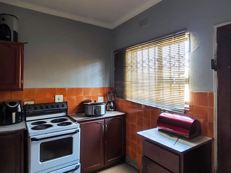 A compact kitchen featuring dark wood cabinetry, orange tiled splashbacks, and a freestanding stove, requiring some cosmetic updates to the wall finishes.