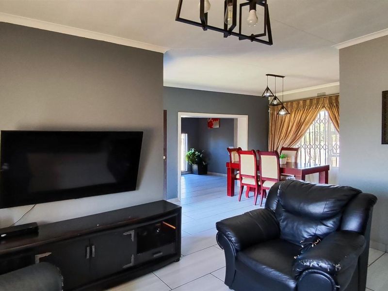 Open-plan living and dining area featuring neutral grey walls, tiled flooring, and direct access to an adjacent room through a wide doorway.