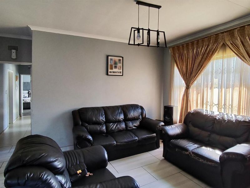 A well-lit living room featuring neutral grey walls, tiled flooring, and a modern pendant light fixture, providing a comfortable and functional space.