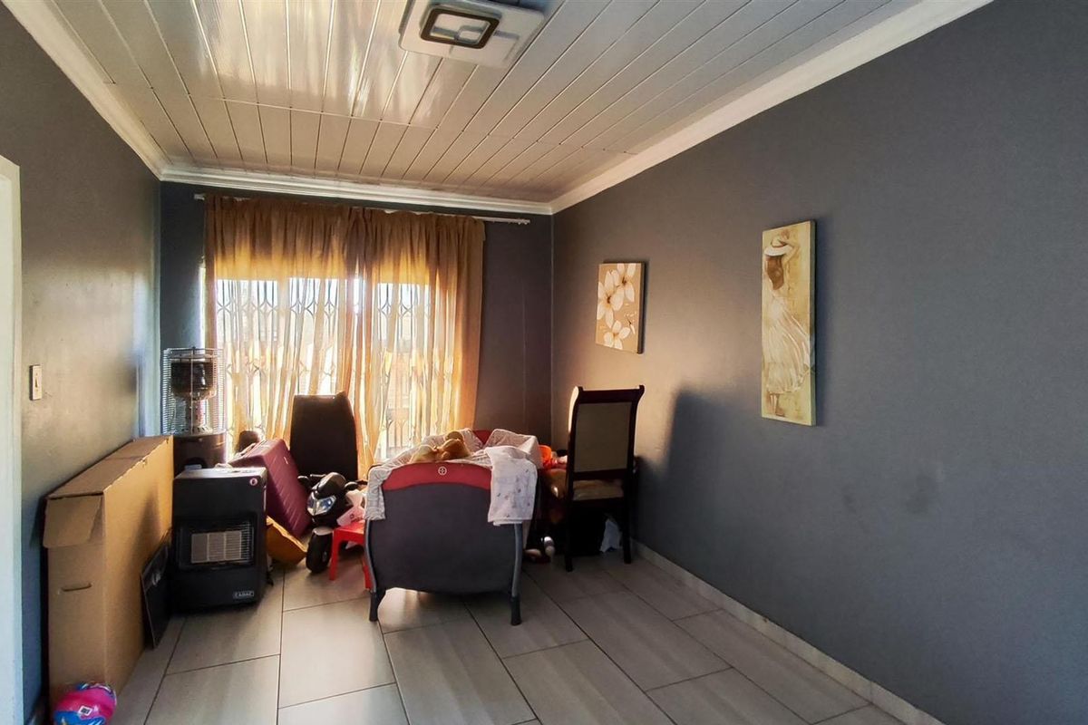 A living room featuring tiled flooring, a tongue and groove ceiling, and a sliding door with a security gate.