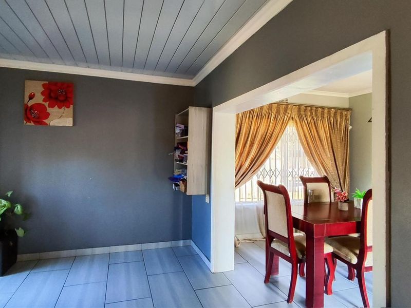 Open plan living and dining area featuring tiled flooring, a tongue and groove ceiling, and a security gate on the window.