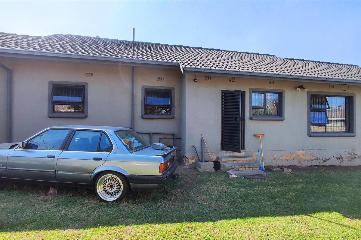 Rear exterior view of the house featuring a tiled roof, security-fitted windows, and a rear entrance door with visible exterior wall maintenance required.