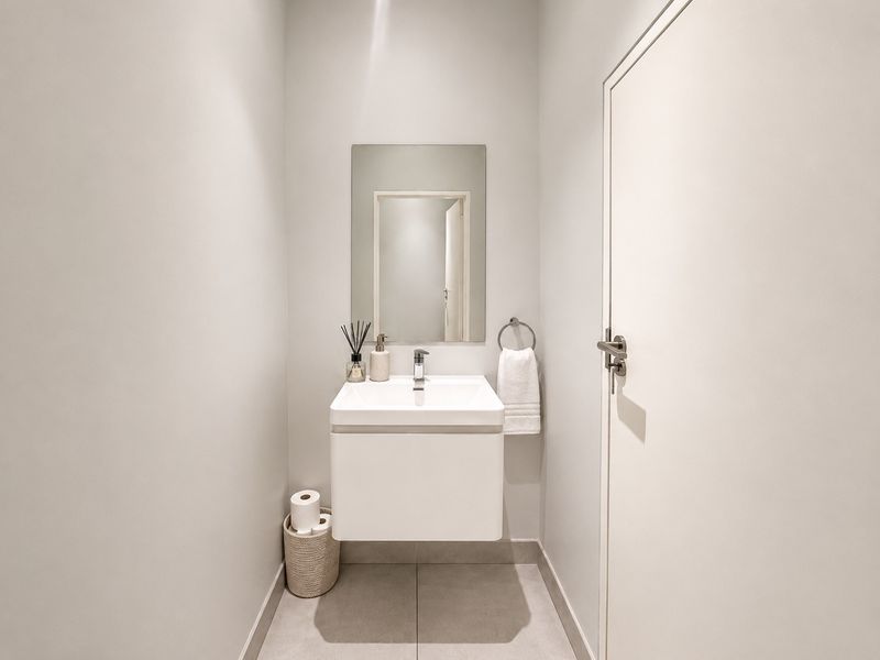 A modern, minimalist powder room featuring a wall-mounted vanity, basin, and sleek mirror, finished with neutral floor tiles.