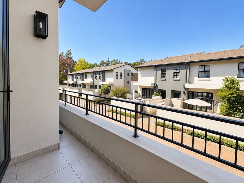 A clean, modern balcony featuring tiled flooring and a black metal balustrade, overlooking a well-maintained residential complex.