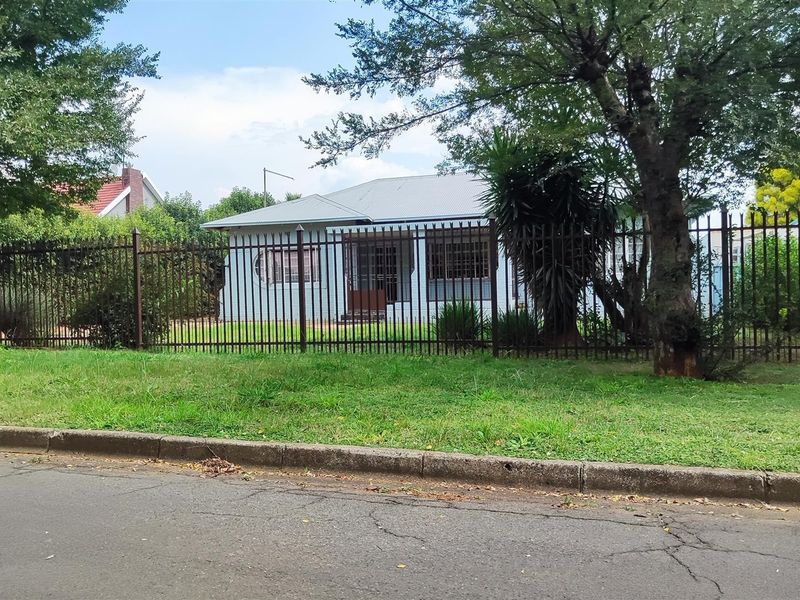 Front view of a residential house featuring a metal security fence, a corrugated metal roof, and a well-maintained front garden area.