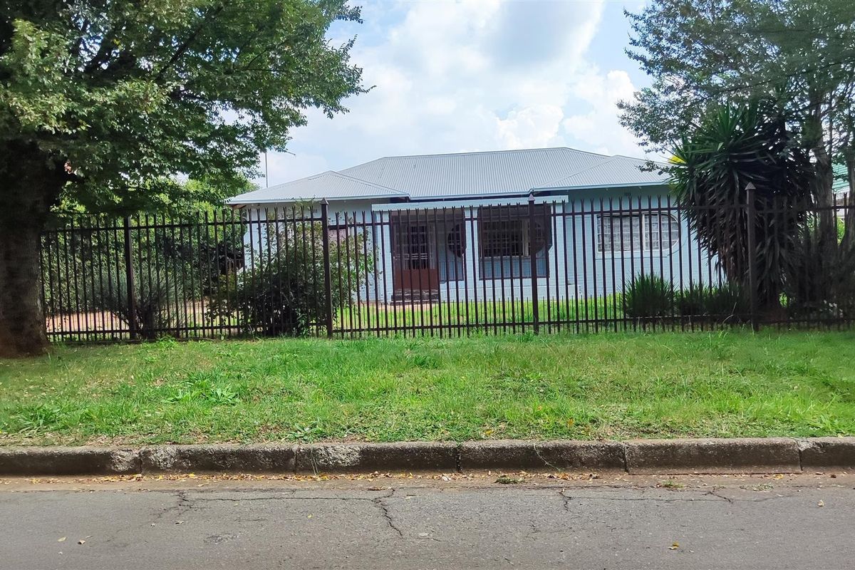Front view of a single-story residential house featuring a metal roof and secure perimeter fencing, set back from the street.