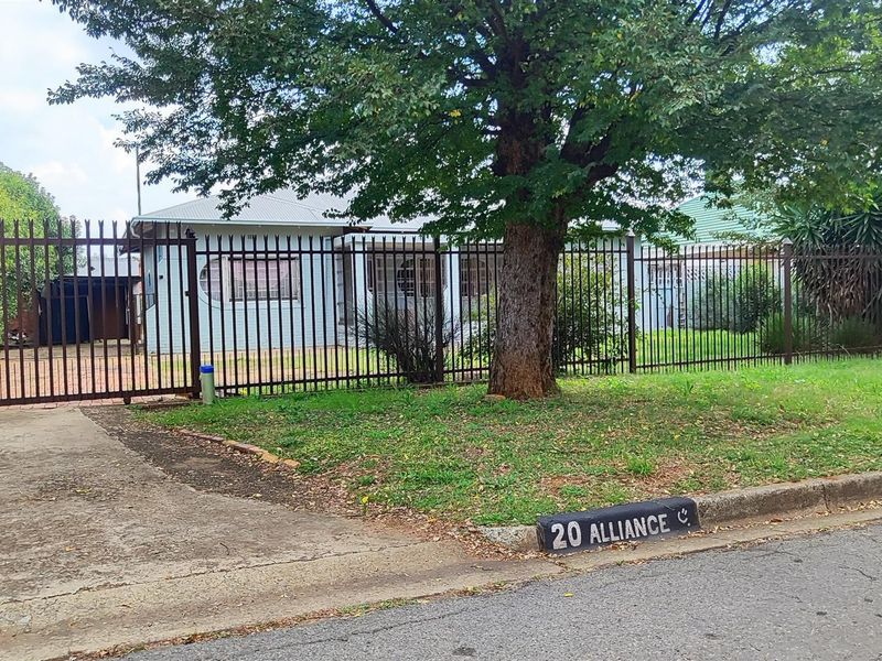 Front view of a residential property featuring a metal security fence, sliding gate, concrete driveway, and a brick facade with a tiled roof.